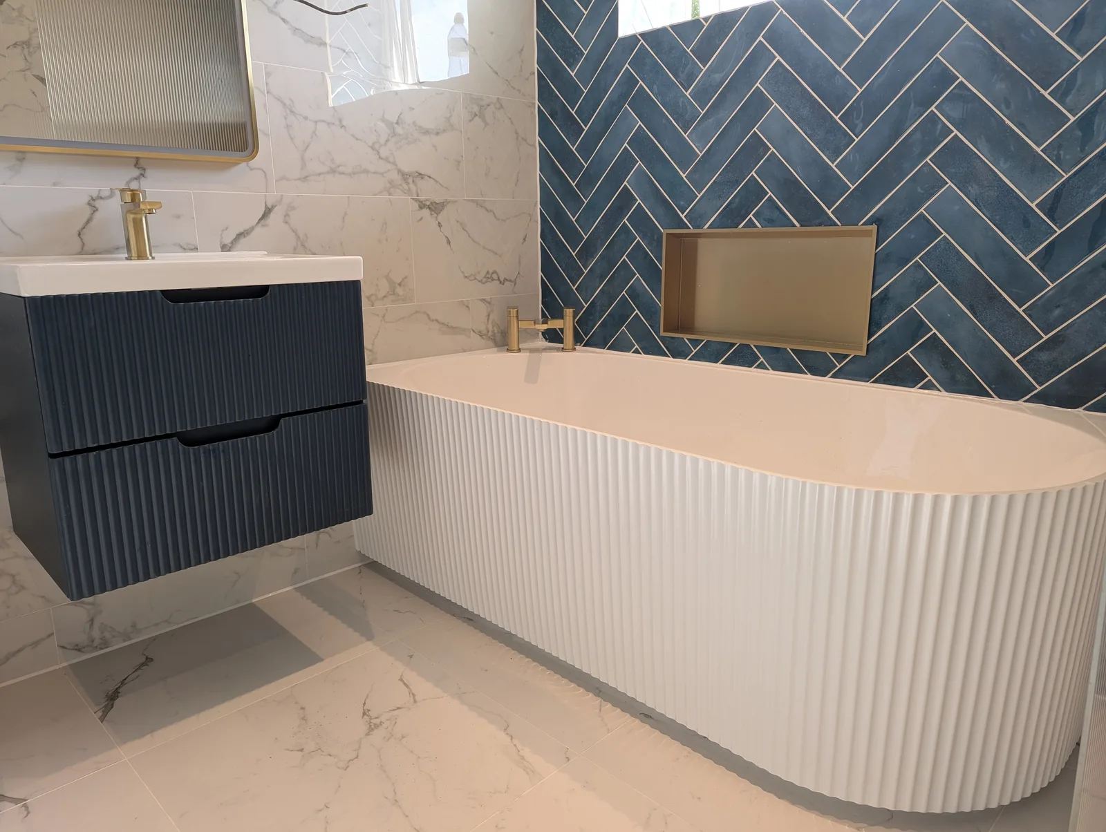 Blue herringbone feature wall with fluted freestanding bath and brass fixtures, fitted by GWS