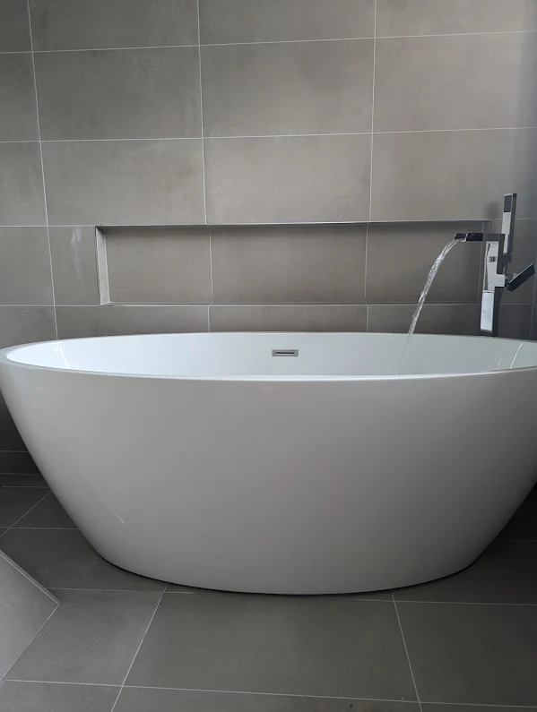 Elegant freestanding white bath with grey tile surround