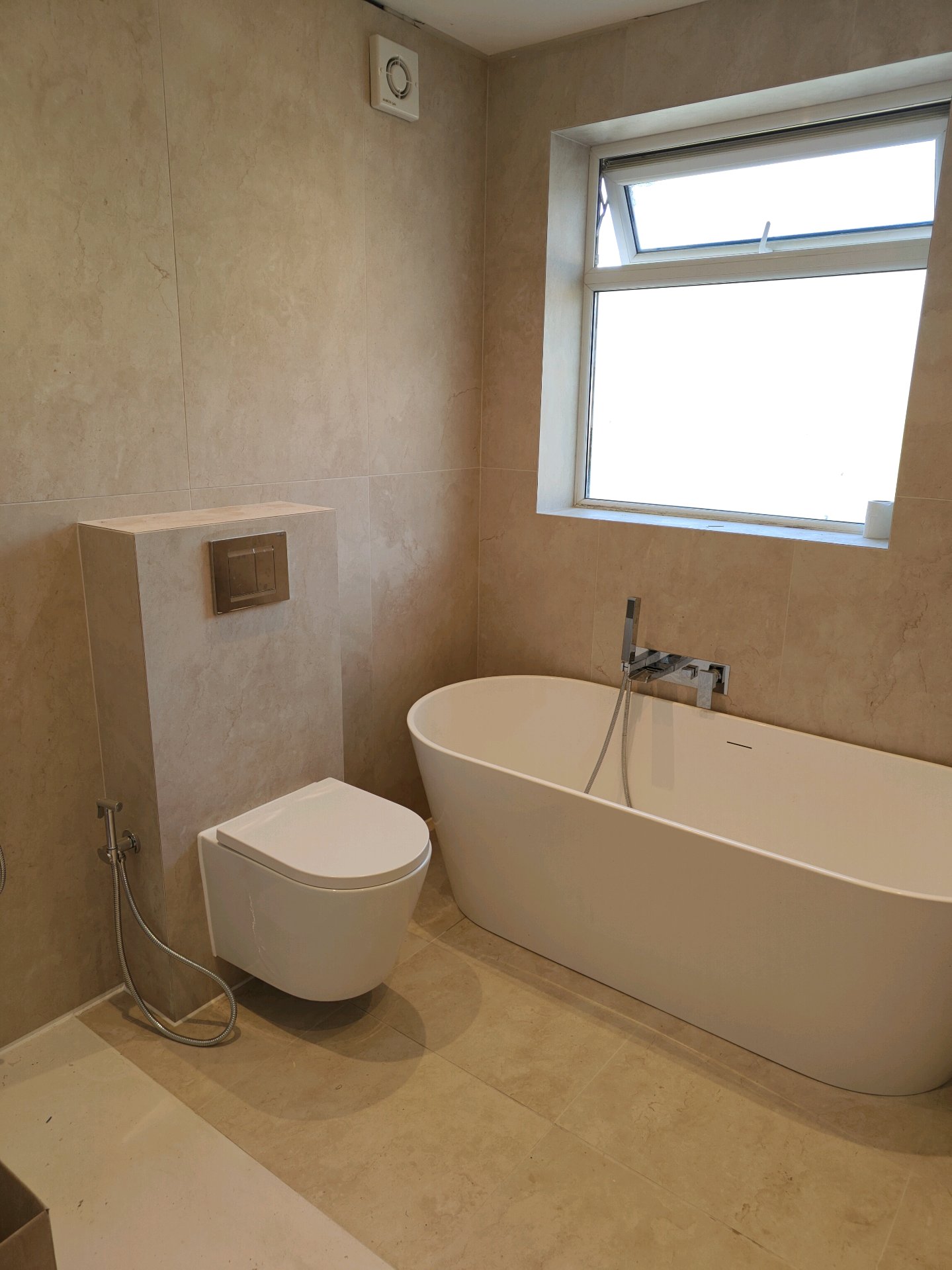 Sandstone bathroom with freestanding tub, wall-hung toilet and bidet spray